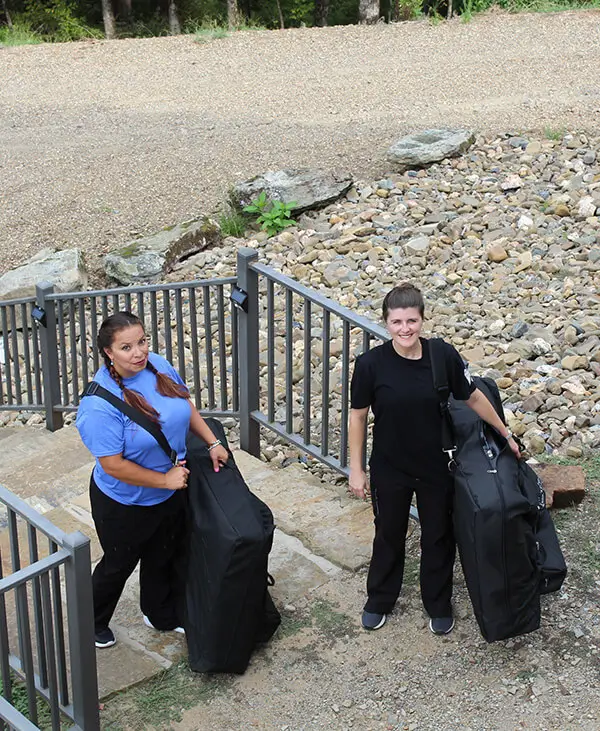 Two massage therapists carrying portable massage tables to a cabin. 