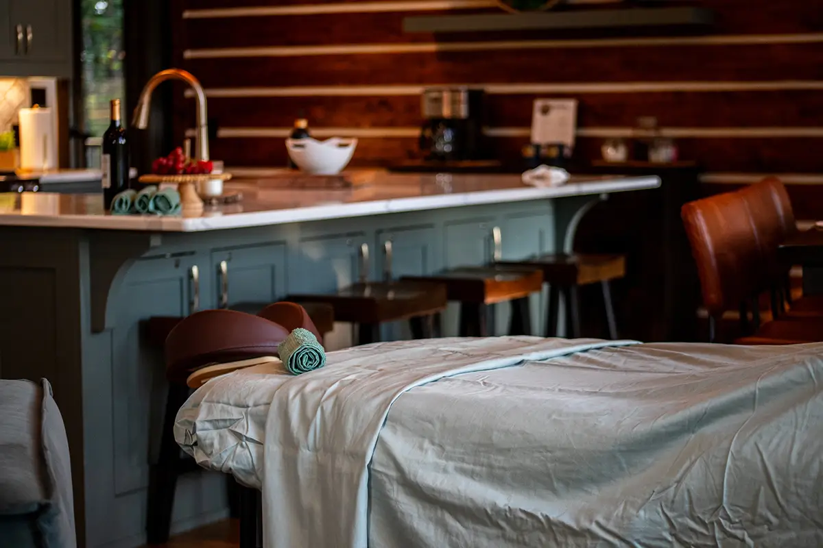 Massage table with folded towels set up in a modern kitchen space, creating a cozy home spa atmosphere.