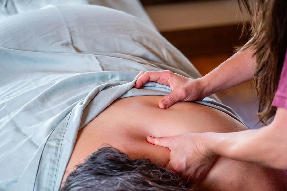 Massage vs. Stretching: Which Is Better for Tight Muscles? | A Servants Hands Massages A massage therapist uses their thumbs to apply pressure to a client's upper back and neck.